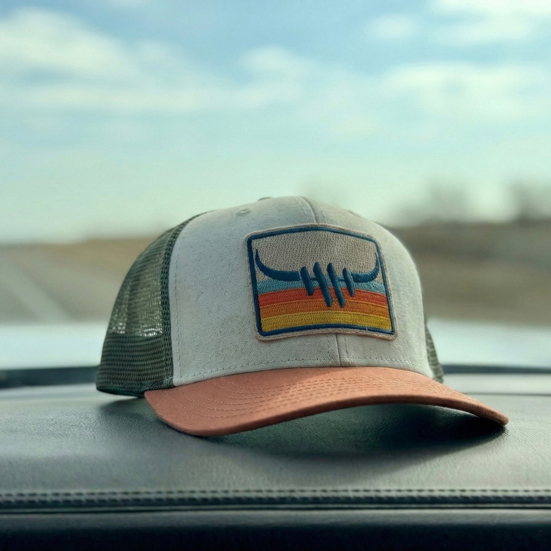 Trucker hat with a logo on a car dashboard with a road and sky in the background
